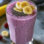 A thick, creamy berry banana Greek yogurt smoothie in a clear tall glass with fresh fruit and a straw, natural morning light, wooden background.